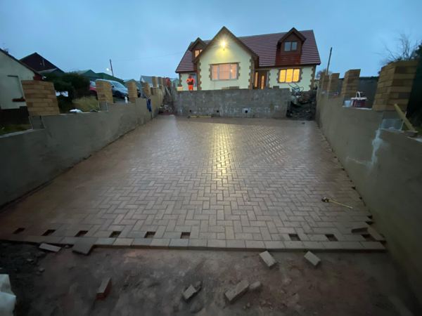 A red herringbone driveway at dusk, between new block walls and brick piers