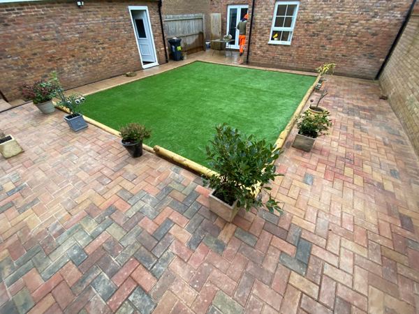 Herringbone block paving around an artificial lawn in a small walled courtyard
