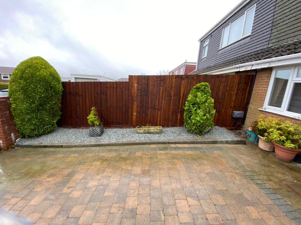 Finished dark-stained close-board fence behind a gravel bed and block-paved drive