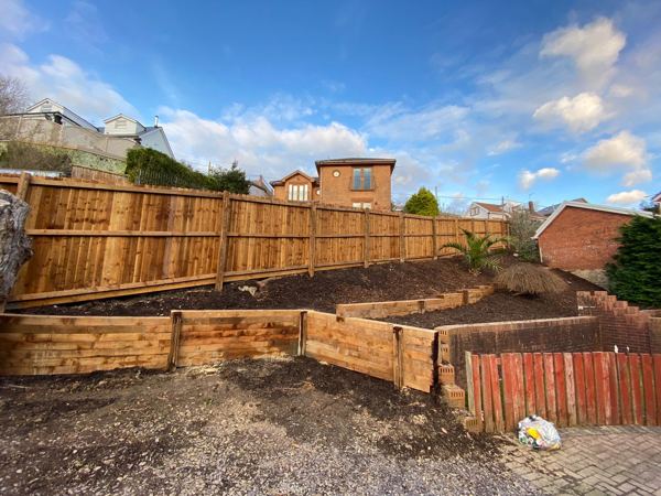 Terraced beds held by sleeper walls, with the new close-board fence along the top