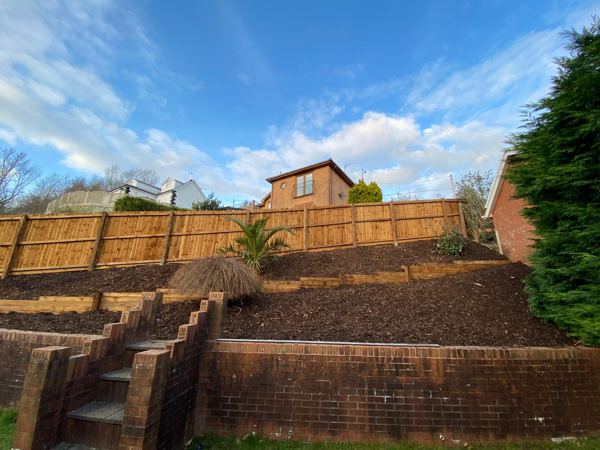 Mulched terraces above the old brick steps, with the fence stepping down the bank