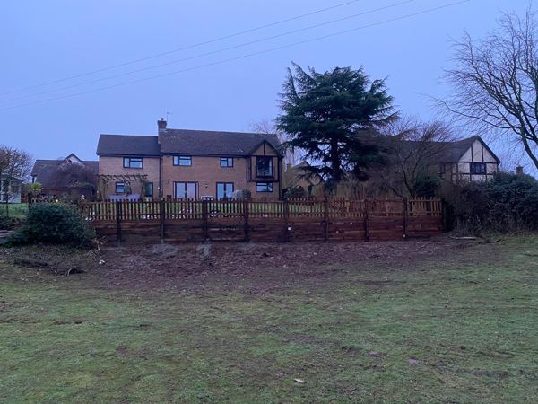 Finished timber retaining edge with picket fence above, seen from the grass below