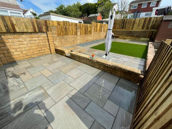 A finished garden: grey sandstone patio, buff brick walls and raised artificial lawn