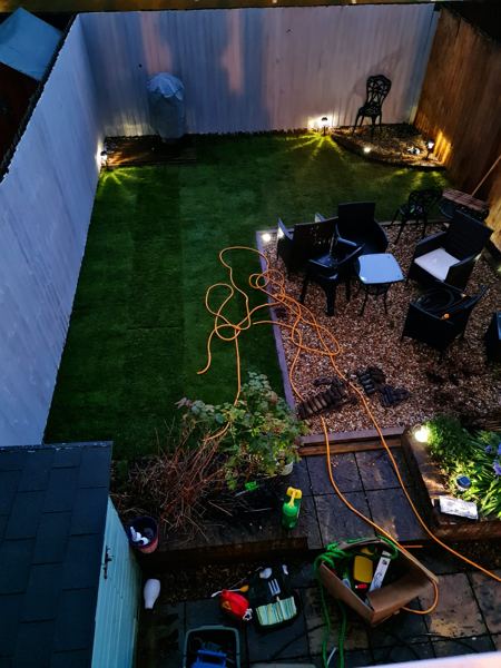 After, at dusk: fresh turf, gravel seating area and small lights along the back