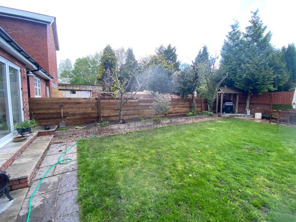 Finished horizontal sleeper fence behind a border of young fruit trees