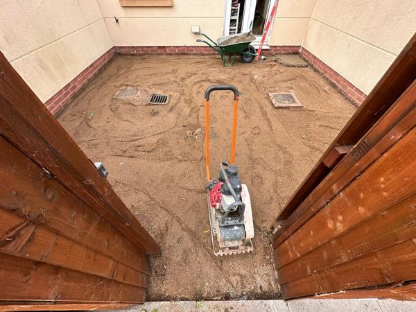 The courtyard base levelled and ready, with the plate compactor and drain covers