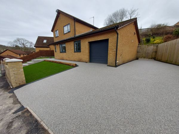 Finished resin driveway beside the garage, with artificial grass and a brick pier