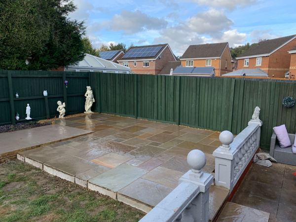 The raised patio edge above the lawn, with the green close-board fence behind