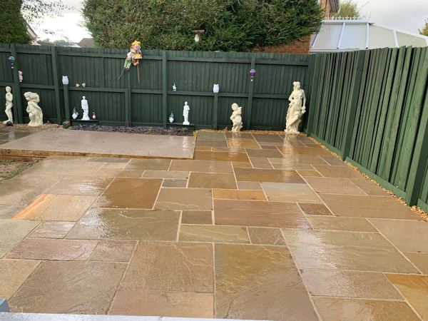 The finished sandstone patio after rain, with the higher platform along the fence