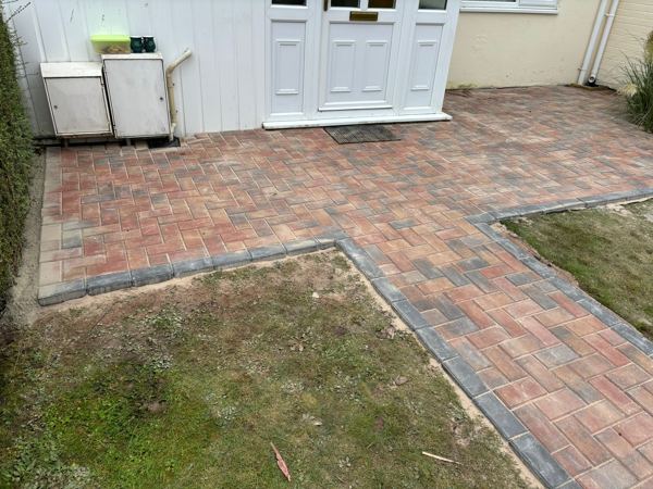 The wider paved area at the door, reaching round to the meter boxes