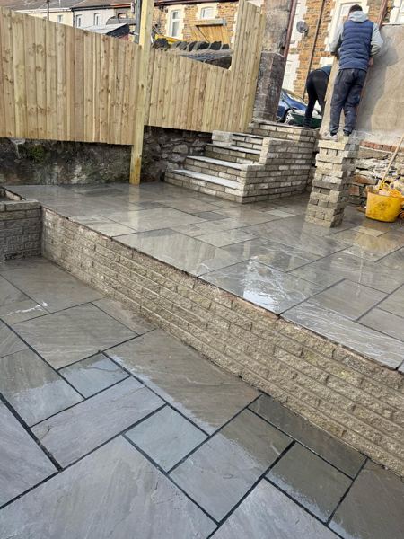 Two paved levels and the retaining wall, with a stone pillar being built at the top