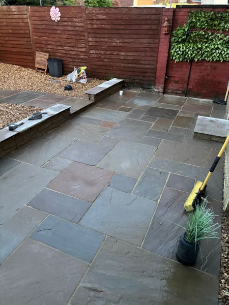 The finished sandstone patio beside the house, with gravel above the low brick wall